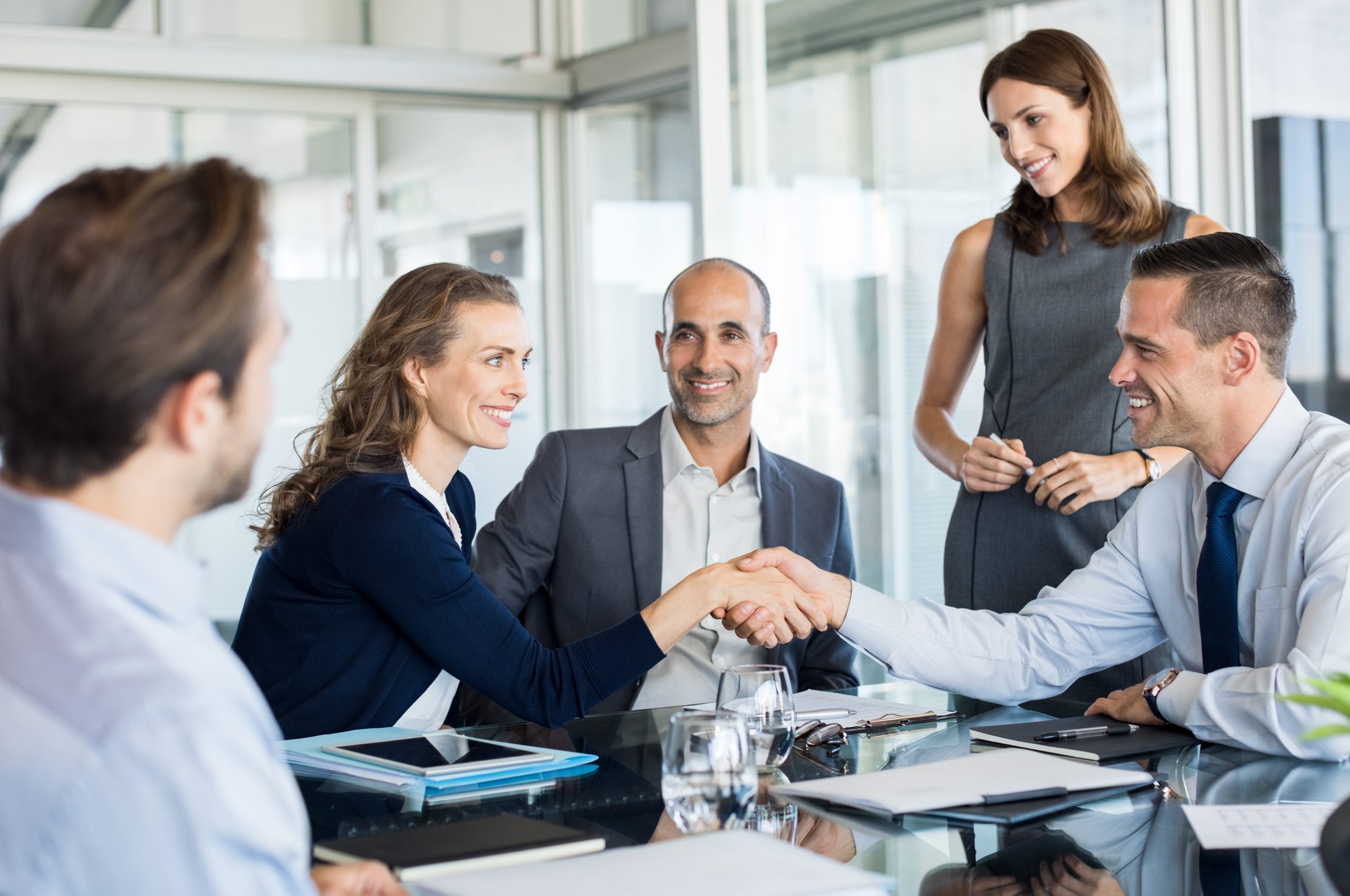 Handshake to seal a deal after a meeting. Two successful business people shaking hands in front of their colleagues. Mature businesswoman shaking hands to seal a deal with smiling businessman.